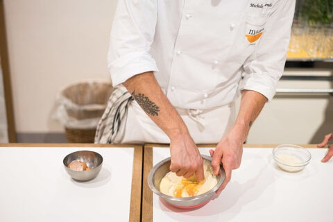 a chef mixing flour and eggs in a steel bowl